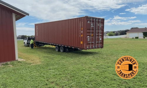 Red container being unloaded in a grass field.