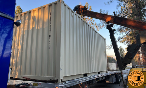 Crane lifting container on a flatbed trailer for transport.